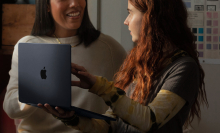 woman holding apple m1 macbook air and talking with another woman