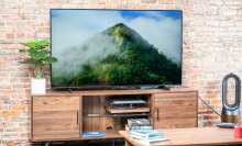 The 50-inch AU8000B Smart TV from Samsung standing on top of living room shelving surrounded by a plant and accessories
