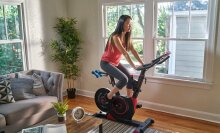 A woman riding an Echelon EX-3 bike in her living room in front of some windows