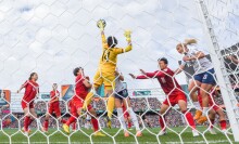 Two teams battle for a soccer ball in front of a white net.