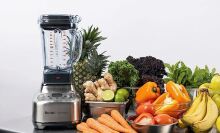 The Breville Super Q Pro standing next to a wide variety of fruits and vegetables