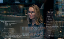 A woman looking at a computer screen with multiple bits of code and data artfully overlaid on the image