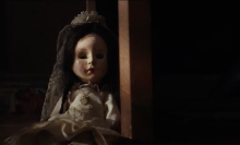 A small doll is seen wearing a white dress.