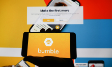 Bumble app logo is displayed on a mobile phone screen photographed on Bumble website background