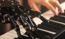 a robotic hand and a human hand playing a piano together