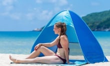 Woman sitting in front of a POP-A-SHADE tent in a blue color on a sandy beach.