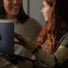 woman holding apple m1 macbook air and talking with another woman