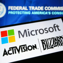 Microsoft and Activision Blizzard logos are seen on a smartphone in front of the Federal Trade Commission (FTC) logo on a PC screen. 