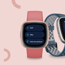 Two Fitbit Versa smartwatches on a pink background