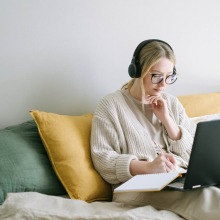 woman taking notes while using laptop