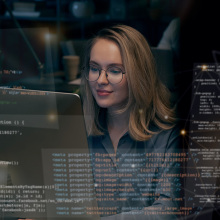 A woman looking at a computer screen with multiple bits of code and data artfully overlaid on the image