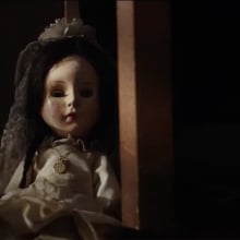 A small doll is seen wearing a white dress.