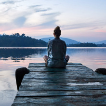 A woman sitting on a dock while watching the sunset over a lake.