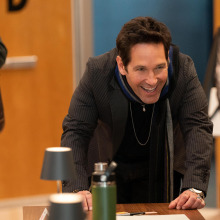 A man smiles while leaning down to talk to a woman during a table read. 