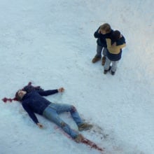 Seen from above, a man lies dead in the snow, while a woman and young boy stand shocked.