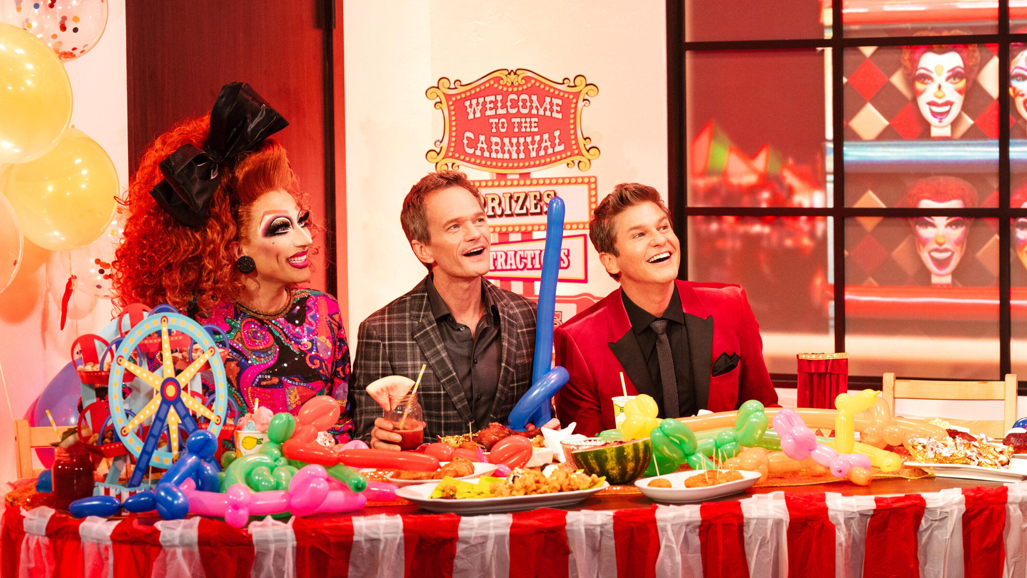 A drag queen and two men sit at a carnival-themed dinner table. 