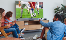 a group of people watching a soccer game on a tv controlled by a fire tv cube in a gray living room