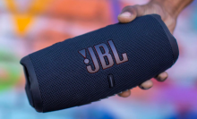 a close-up of a person holding a jbl charge 5 in front of a colorful wall
