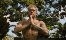 Jake Paul, shirtless, with his eyes closed and hands in prayer. Trees are behind him.