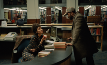 A man and a woman talk in a library. 