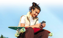 woman with a longboard on lap looking down at cell phone