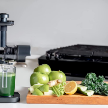 ninja neverclog cold press juicer to the left. green apple, orange, kale, and cucumber to the right.