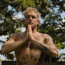 Jake Paul, shirtless, with his eyes closed and hands in prayer. Trees are behind him.