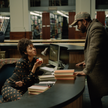 A man and a woman talk in a library. 