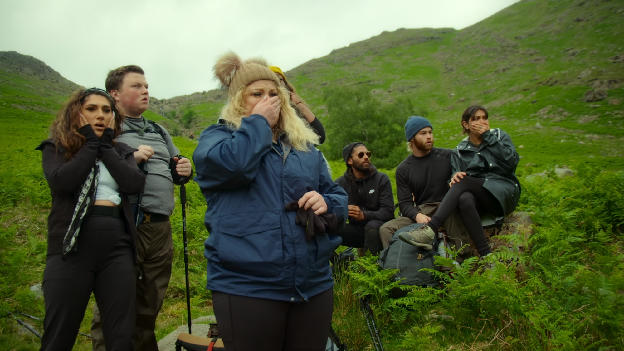 A group of people look shocked while hiking on a green hill. 