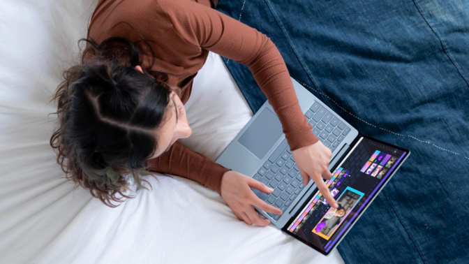 a top-down view of a girl using a microsoft surface laptop go 2 on a bed with a denim quilt