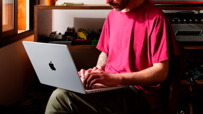 a man wearing a red shirt in a recording studio working on an m2 max-equipped apple macbook pro